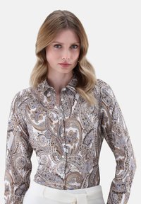 Camicia a maniche lunghe bianca con un intricato motivo paisley in beige, blu e marrone. Presenta un colletto e chiusura con bottoni.