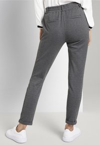 Spodnie w szaro-czarny wzór w zębatkę z elastycznym pasem, zwężającym się krojem i pięcioma kieszeniami, w połączeniu z białymi trampkami na neutralnym tle.