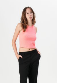 Haut court rose ajusté à côtes avec un col rond et une conception sans manches, associé à un pantalon noir ajusté. Texture lisse et coutures minimales.