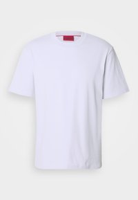 Biała koszulka typu T-shirt z krótkim rękawem, okrągłym dekoltem i subtelnym wytłoczonym logo na klatce piersiowej, z czerwoną metką wewnętrzną na dekolcie, zaprezentowana na jednolitym tle.