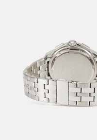 Montre en acier inoxydable argenté avec un bracelet à maillons, un boîtier rond et une couronne texturée. Présente une finition lisse et polie.