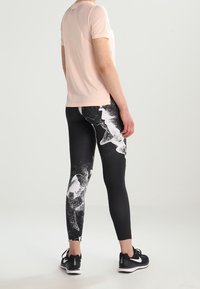 Top sportivo a maniche corte di colore rosa chiaro abbinato a leggings neri con un motivo astratto bianco. Sneakers nere completano l'outfit.
