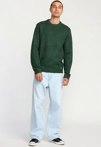 Skogsgrön stickad tröja med rund halsringning, ribbade muddar och fåll. Kombinerad med ljusblåa vida jeans och svarta sneakers.