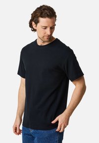 Black short-sleeve t-shirt in smooth cotton fabric, featuring a classic crew neckline and relaxed fit, paired with blue denim jeans.