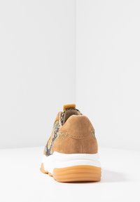 Baskets avec un talon en suède beige et une tige imprimée motif serpent, équipées d'une semelle intermédiaire blanche et d'une semelle extérieure en caoutchouc marron. Design moderne avec languette de tirage.