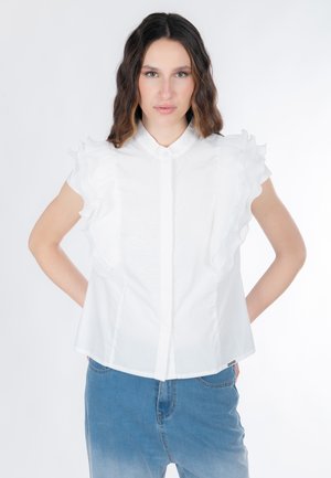 Blusa bianca a maniche corte con dettagli arricciati sulle spalle, con chiusura frontale a bottoni e vestibilità casual. Abbinate a jeans blu.