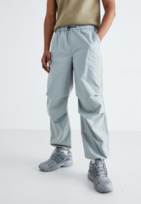 Light blue, loose-fitting pants with an elastic waistband, featuring side pockets and a smooth texture. Paired with grey athletic shoes.