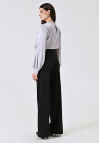 Grau satinierte Bluse mit Puffärmeln und einem Schlüsselaugen-Detail im Rücken, kombiniert mit hoch taillierten schwarzen weit geschnittenen Hosen.