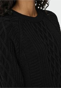 Pull en laine noire avec un motif texturé composé de torsades en relief et un col côtelé. Vue rapprochée mettant en valeur la profondeur et le motif du tissu.