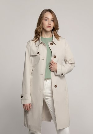 Beiger Trenchcoat mit Kragen, braunen Knöpfen und langen Ärmeln. Trägt man über einem hellgrünen Top und weißen Hosen, was ein elegantes Design zeigt.