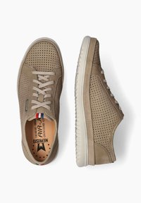 Baskets en cuir beige avec un design perforé, bout rond et semelle texturée. Elles présentent des lacets beige et un petit accent tricolore sur le côté.