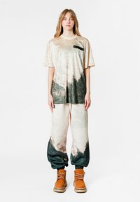Camiseta de terciopelo en color beige claro con un acento negro y un patrón degradado en gris oscuro; combinada con pantalones crema que tienen un dobladillo en gris oscuro y puños elásticos.