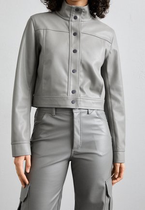Persona que lleva una chaqueta crop de piel sintética gris con botones negros y pantalones de talle alto a juego con bolsillos laterales tipo cargo.
