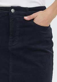 Mornarsko modra ženska krila iz kordiraja s telesu prilegajočim krojem, sprednjim žepom in kovinskim gumbom v pasu, z gladko teksturo.