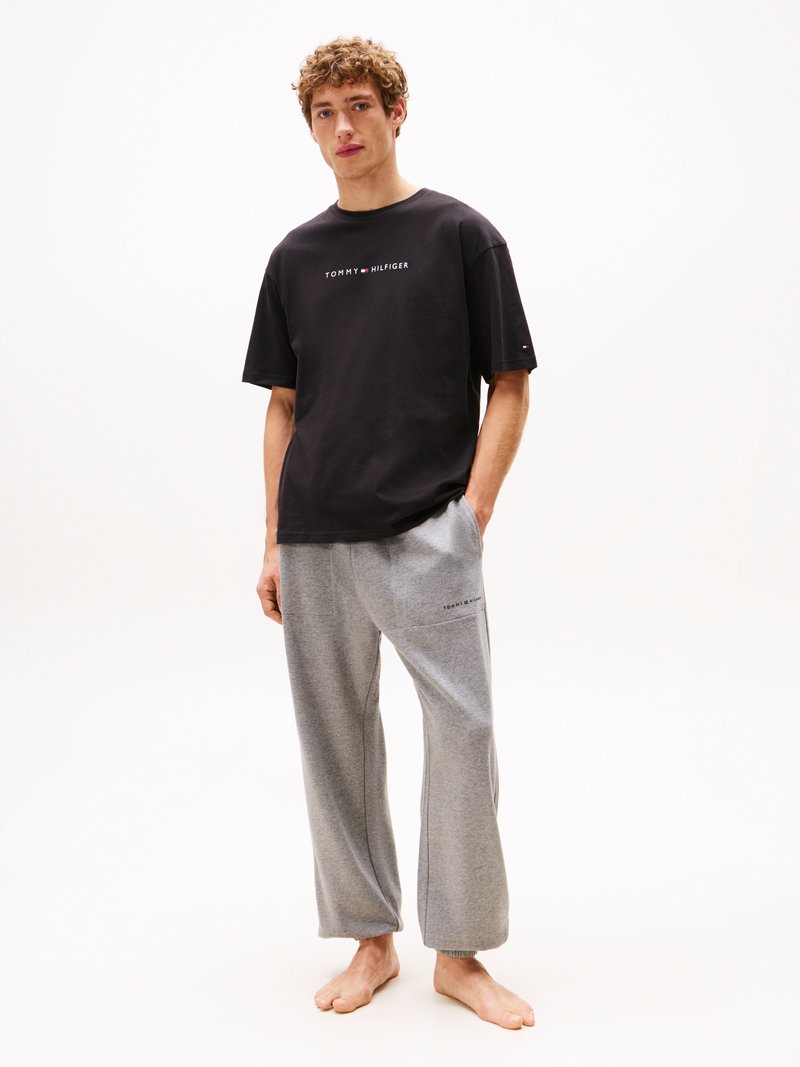 T-shirt en coton noir avec "TOMMY HILFIGER" imprimé en blanc. Pantalons de survêtement gris, coupe décontractée avec des poignets élastiques, comportant des détails de logo.
