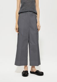 Gray wide-leg trousers with a smooth texture, featuring a high waist and two front pockets; paired with black slip-on sandals.