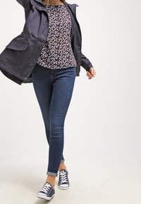 Navy lightweight jacket over a floral-patterned top with blue and white leaves, paired with dark skinny jeans and navy sneakers.