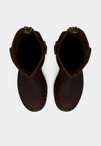 Ζεύγος σκούρων καφέ δερμάτινων μποτών με κίτρινα ραφτικά και μαύρες λαστιχένιες σόλες, σε λευκό φόντο, φωτογραφημένο από πάνω.