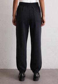 Zwarte joggingsbroek van zacht materiaal, met een elastische tailleband en enkelboorden, voorzien van een enkele achterzak.