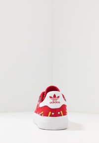 Rote Leinenschuhe mit einem bunten Muster, weißer Gummisohle und einem gebrandeten Fersenpatch mit Logo. Strukturierte Oberfläche im Obermaterial.