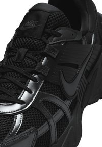 Black Nike sneakers featuring a mesh upper, smooth synthetic accents, intricate stitching, and a textured sole with prominent branding.