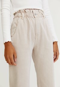 Pantalon beige clair taille haute avec taille élastique, poches latérales et coupe décontractée. Texture douce et détails de couture subtils.
