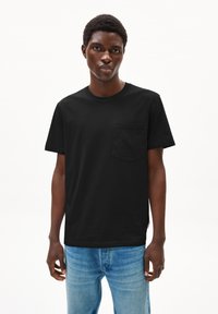 Zwart katoenen T-shirt met korte mouwen, een ronde halslijn en een borstzak. Gecombineerd met lichtblauwe denim jeans.