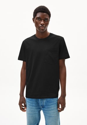 Schwarzes Baumwoll-T-Shirt mit kurzen Ärmeln, Rundhalsausschnitt und einer Brusttasche. Kombiniert mit hellblauen Jeans.