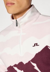 Pullover in pile di colore rosa e bianco con un motivo montano, chiusura a mezza zip e logo ricamato a contrasto sul petto.
