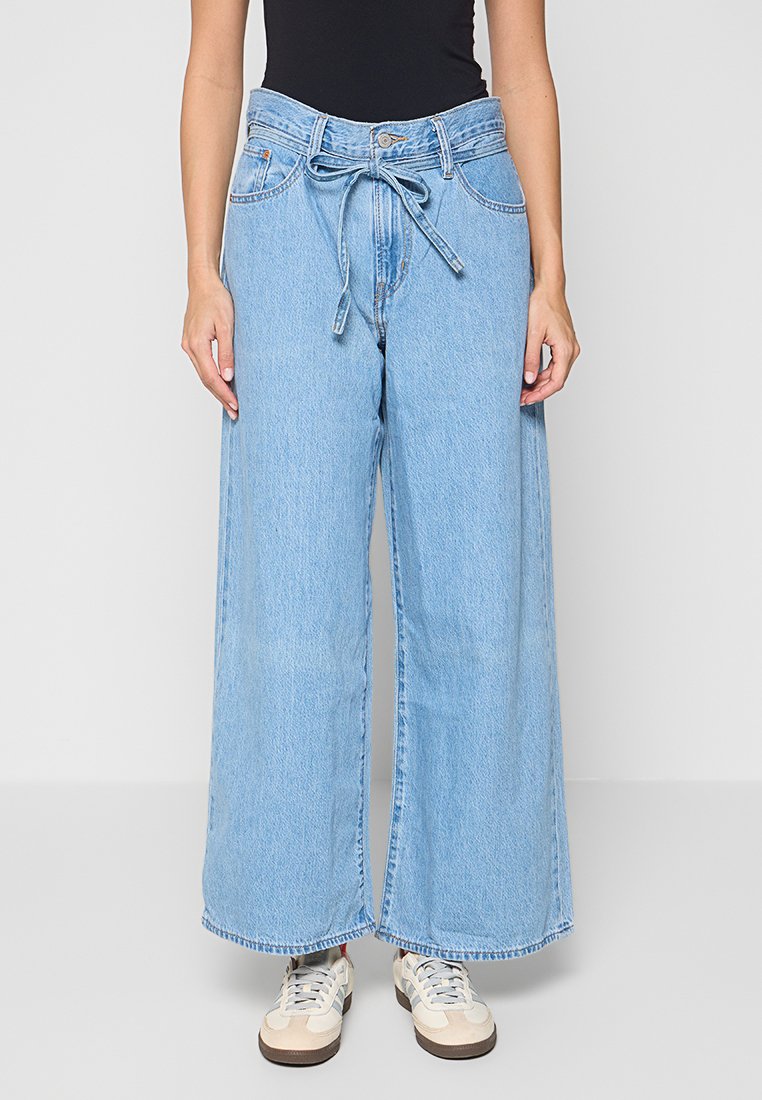 Jean large bleu clair avec ceinture à nouer, en denim. Doté de poches avant et d'une coupe décontractée, complété par des baskets décontractées.