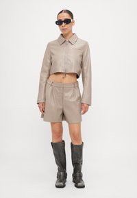 Beige cropped leather jacket with a front zipper, paired with beige leather shorts; model wearing black sunglasses and gray knee-high boots.
