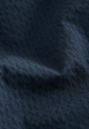 Mørkeblå stof med en struktureret overflade, der har subtile, varierende mønstre og et glat fald. Ideel til tekstiler og polstring.