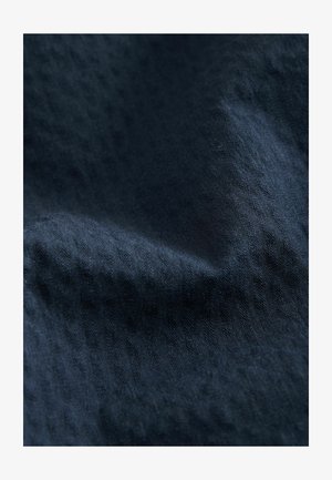 Dunkelblauer Stoff mit einer strukturierten Oberfläche, die subtile, wechselnde Muster aufweist und einen angenehmen Fall hat. Ideal für Textilien und Polsterungen.