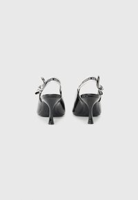 Black patent leather slingback heels with a pointed toe, featuring a mid-height stiletto heel and a patterned strap with logo detailing.