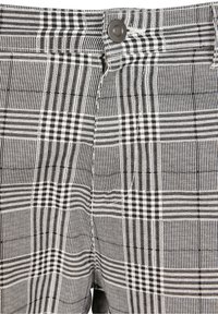 Gros plan sur un pantalon à carreaux noir et blanc taille haute avec une fermeture à bouton et à glissière.