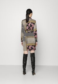 Sukienka z długim rękawem, wykonana z materiału o wielokolorowym wzorze w odcieniach czerni, różu i złota, z paskiem w talii i długości do kolan, w połączeniu z czarnymi kozakami sięgającymi do uda.