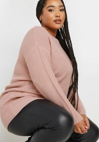 Helles rosa gestricktes Sweatshirt mit einer strukturierten Oberfläche, gerippten Bündchen und lässiger Passform, kombiniert mit schwarzen Leggings aus Kunstleder.