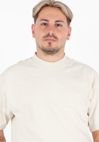Crème t-shirt met korte mouwen met een verhoogd kruispatroon aan de voorkant, ronde halslijn en zachte katoen materiaal.