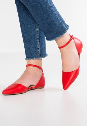 Czerwone skórzane baleriny z ostrymi noskami i paskami na kostkach. Posiadają niski obcas i gładką teksturę, zestawione z dżinsami w niebieskim odcieniu z postrzępionymi końcami.