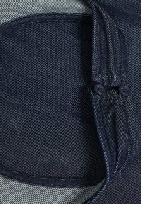 Marinblå denimtyg med en liten cirkulär utskärning, med en kontrasterande ljus innertyg och två mörka knappar på högra sidan.