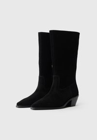 Μαύρες σουέτ μπότες μέχρι το γόνατο με μυτερή μύτη και μέτριο τακούνι. Διαθέτουν ορατή ραφή και λεία υφή.