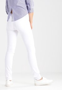 Jeans ajustados blancos con una textura suave, que cuentan con bolsillos traseros y una cintura de altura media, combinados con una camisa a rayas azul y blanca.