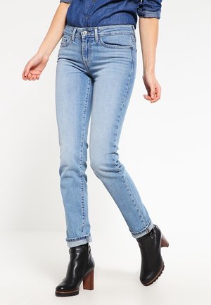 Henkilö, jolla on vaaleansiniset slim fit -farkut, tummansiniset, käännetyt farkkupaita ja mustat nahkaiset nilkkurit, joissa on puiset paksut korot.