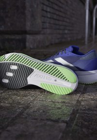 Sininen urheilukenkä, jossa on teksturoitu yläosa, valkoisia yksityiskohtia ja musta-limevihreä pohja, jossa on erottuva kuvio.