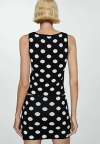 Set a due pezzi a pois bianco e nero in maglia, composto da un top senza maniche e una gonna mini. Tessuto testurizzato con pois rotondi e audaci distribuiti equamente.