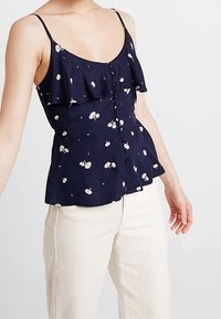 Navy floral peplum top with ruffled straps and button detailing. Features small white and yellow flowers on a smooth fabric.