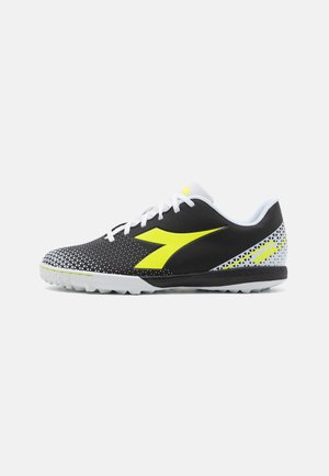 Scarpa sportiva nera con swoosh giallo, upper in mesh con motivo a punti, lacci bianchi e suola in gomma con tacchetti di trazione.