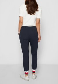 Marina blå joggers med slim fit, elastisk midjeband och vita och röda randiga manschetter. Har en liten bakficka och mjukt material.