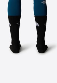 Calcetines negros hasta la rodilla con textura acanalada y detalles de logotipo. El material parece grueso y duradero, adecuado para actividades al aire libre.