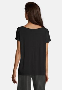 T-shirt nero a maniche corte con vestibilità ampia, scollatura larga e maniche arrotolate. Il tessuto appare liscio, senza motivi o decorazioni visibili.